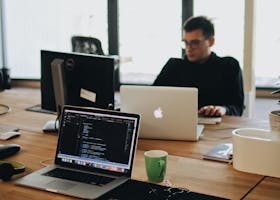 A web developer working on code in a modern office setting with multiple devices.